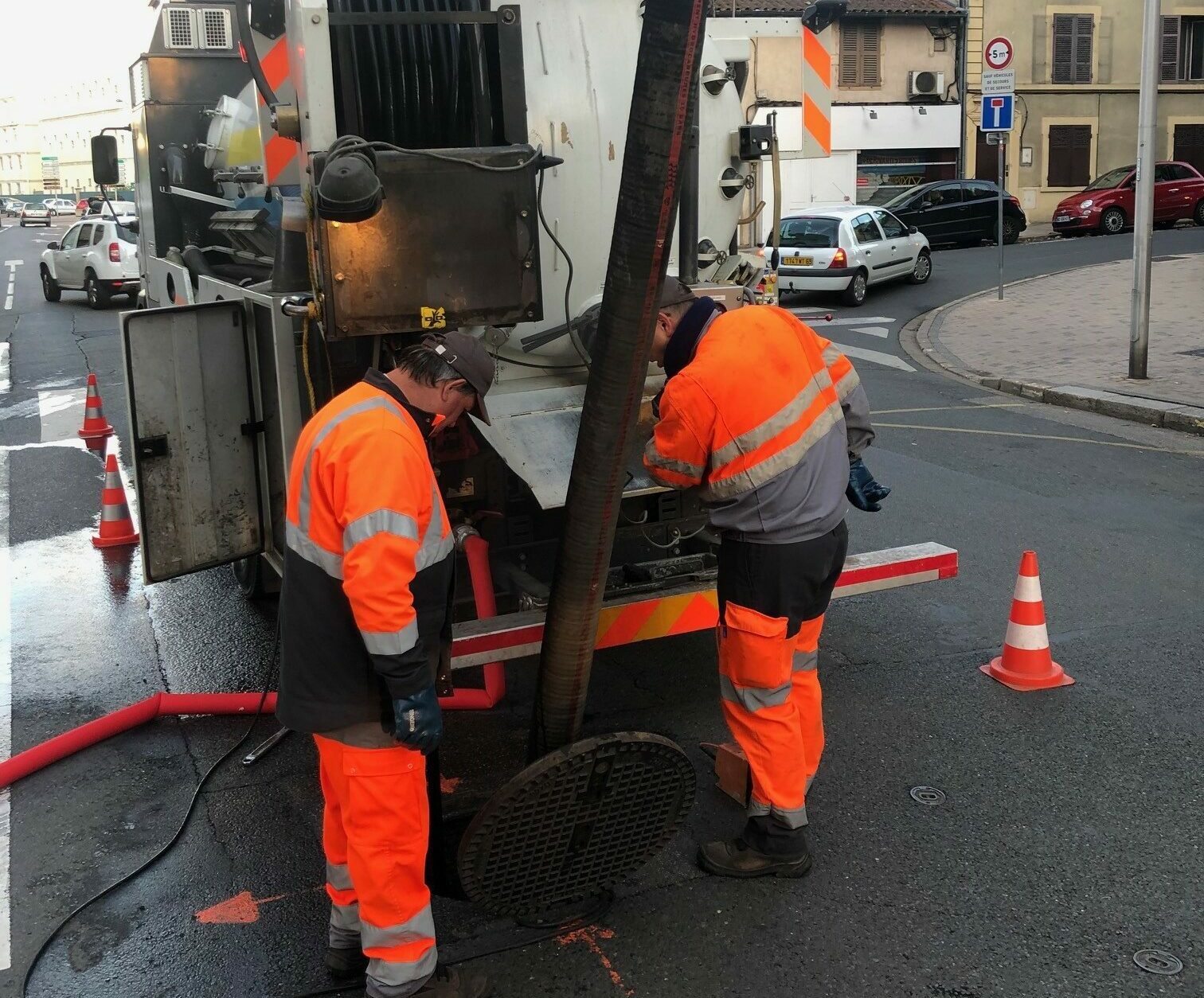 Deux hommes se trouvent à proximité d'un égout dans lequel un tuyau est présent à l'intérieur
