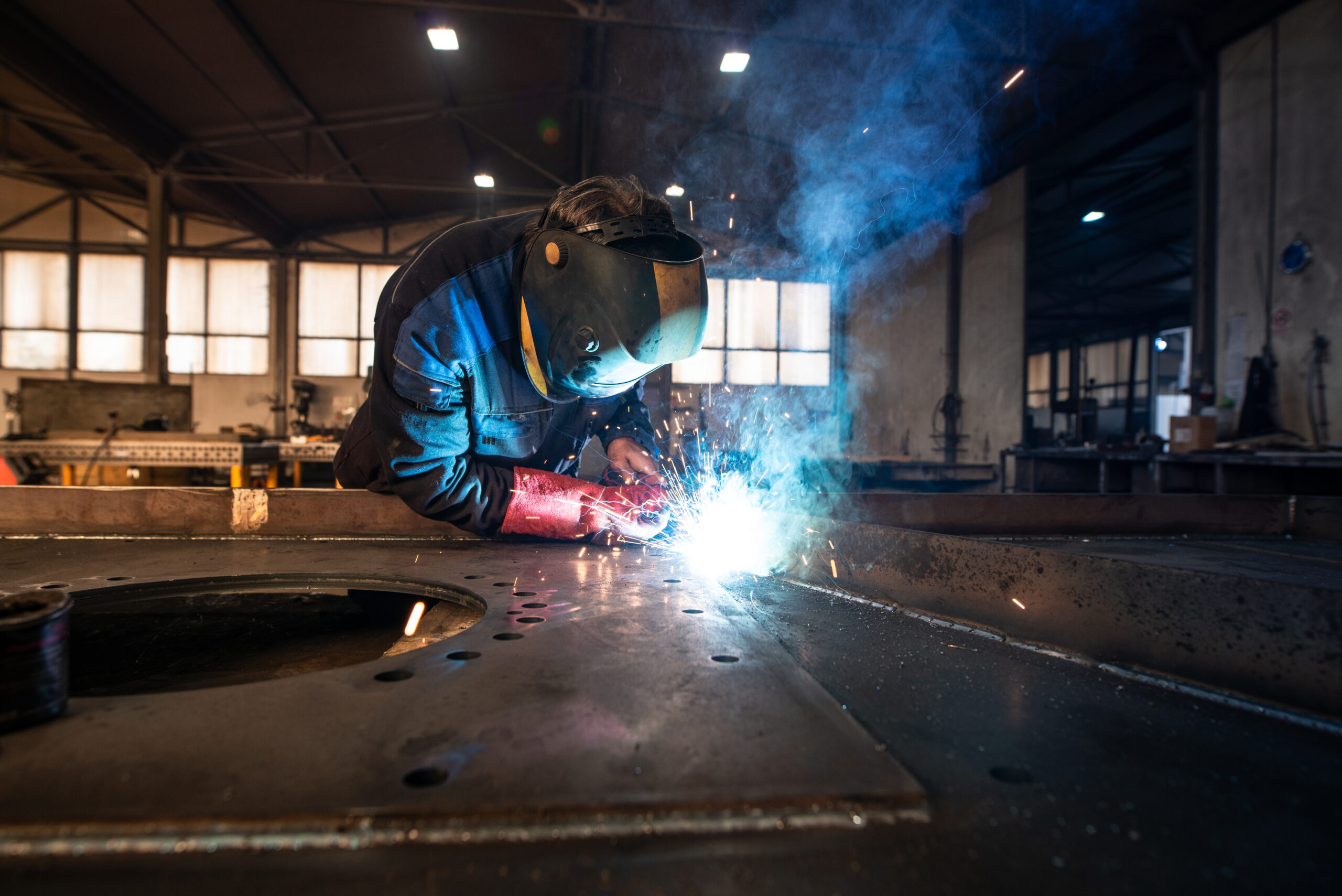 Soudeur industriel professionnel qui soude des pièces métalliques dans une usine de métallurgie.