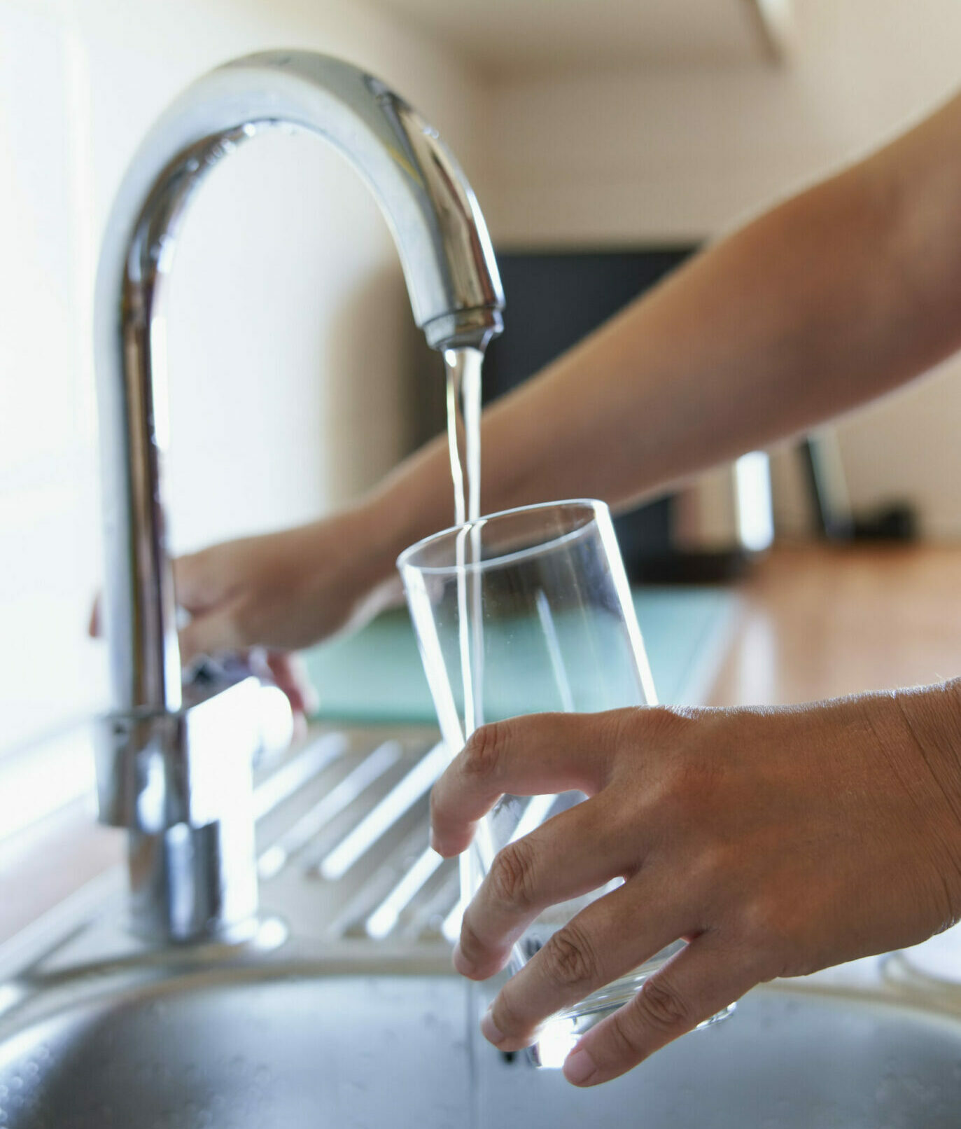 mains de femme remplissant un verre d'eau au robinet d'une cuisine